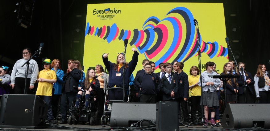 School children stood on stage in front of a yellow Eurovision 2023 banner.